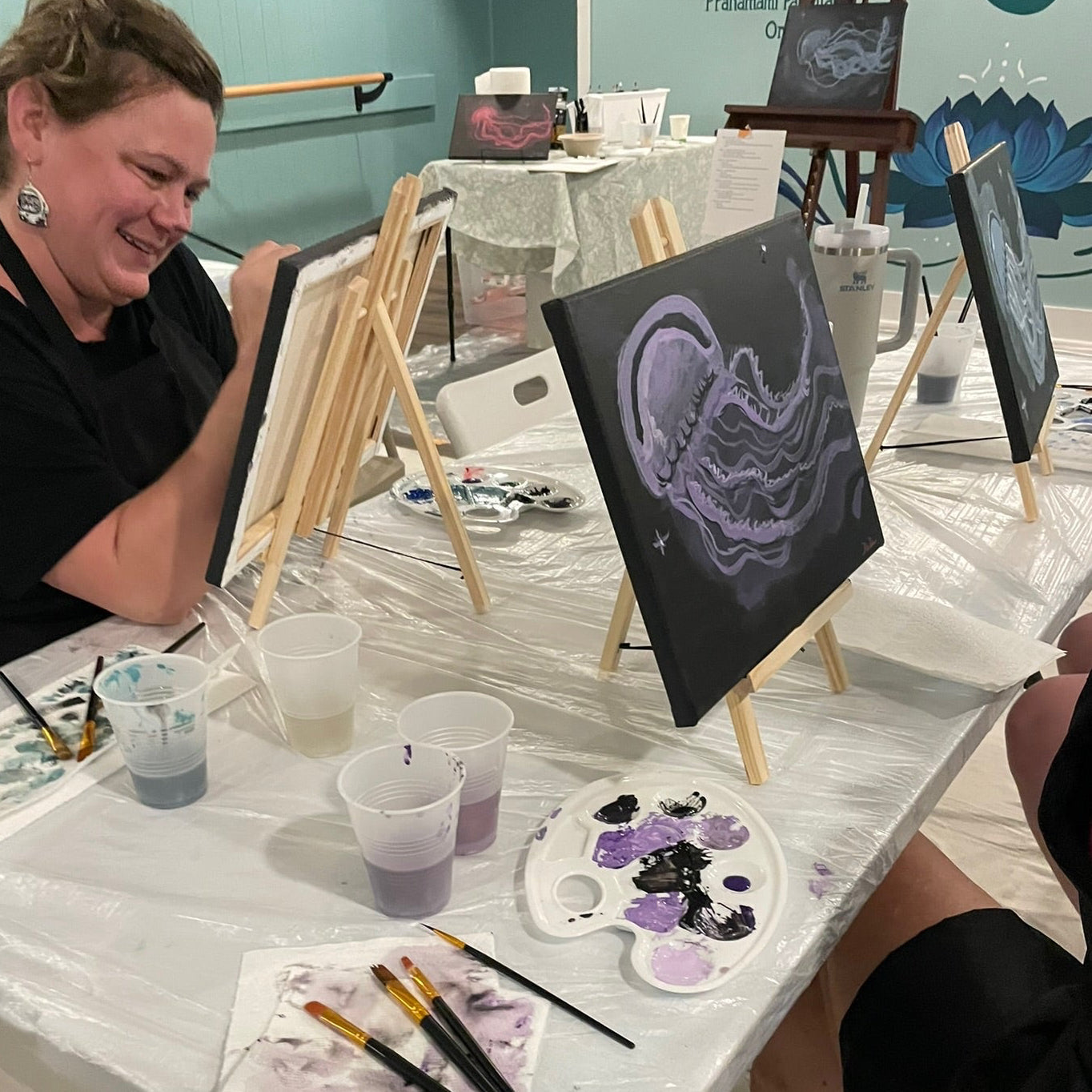 Art class with participants painting jellyfish on canvases at a table.
