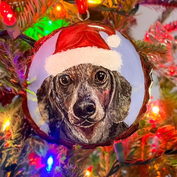 Dog ornament wearing a Santa hat on a Christmas tree with lights.