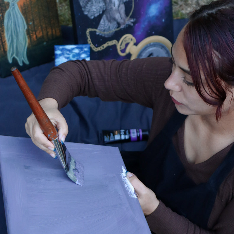 Women painting a purple canvas with a brush in an outdoor setting