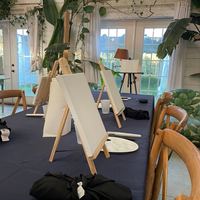 Art class with easels, canvases, and a table covered with a blue cloth.