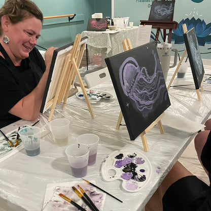 Art class with participants painting jellyfish on canvases at a table.