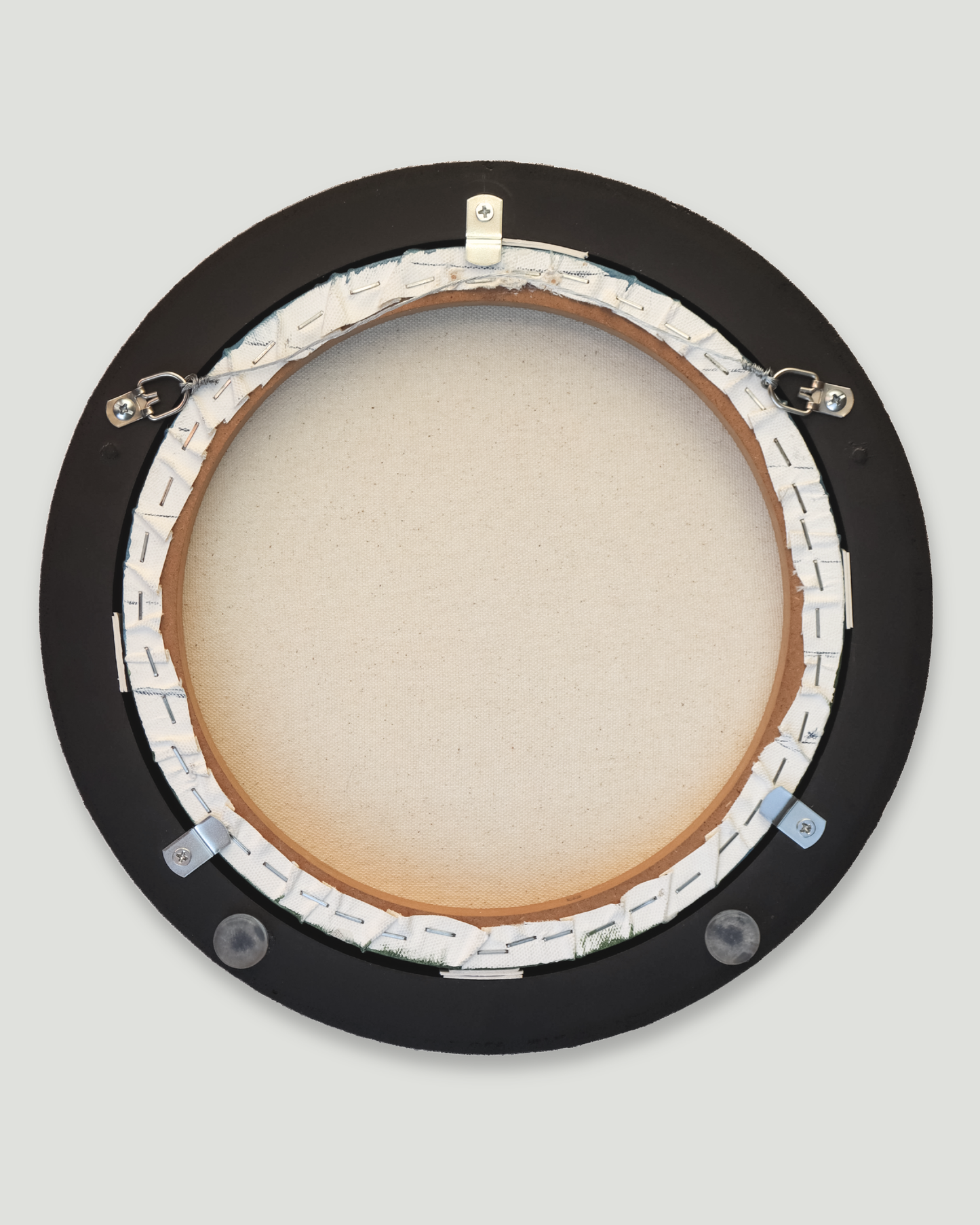 The back view of a circular black-framed wall art piece, showing the canvas wrapped on a wooden stretcher with hanging wires and clips, set against a light gray background.