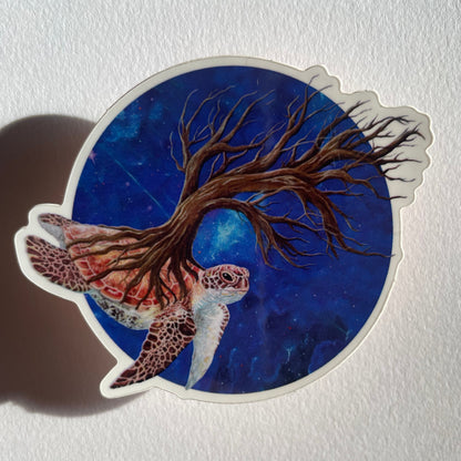 Sticker with a tree and turtle design on a blue background, placed on a textured white surface.